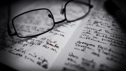 Schwarz-weiß Bild vom inneren eines Notizbuchs in dem beide Seiten voller handschriftlicher Notizen sind. Eine Brille liegt auf der linken Seite, ein Wort scheint rot nachgezeichnet zu sein: Toronto.